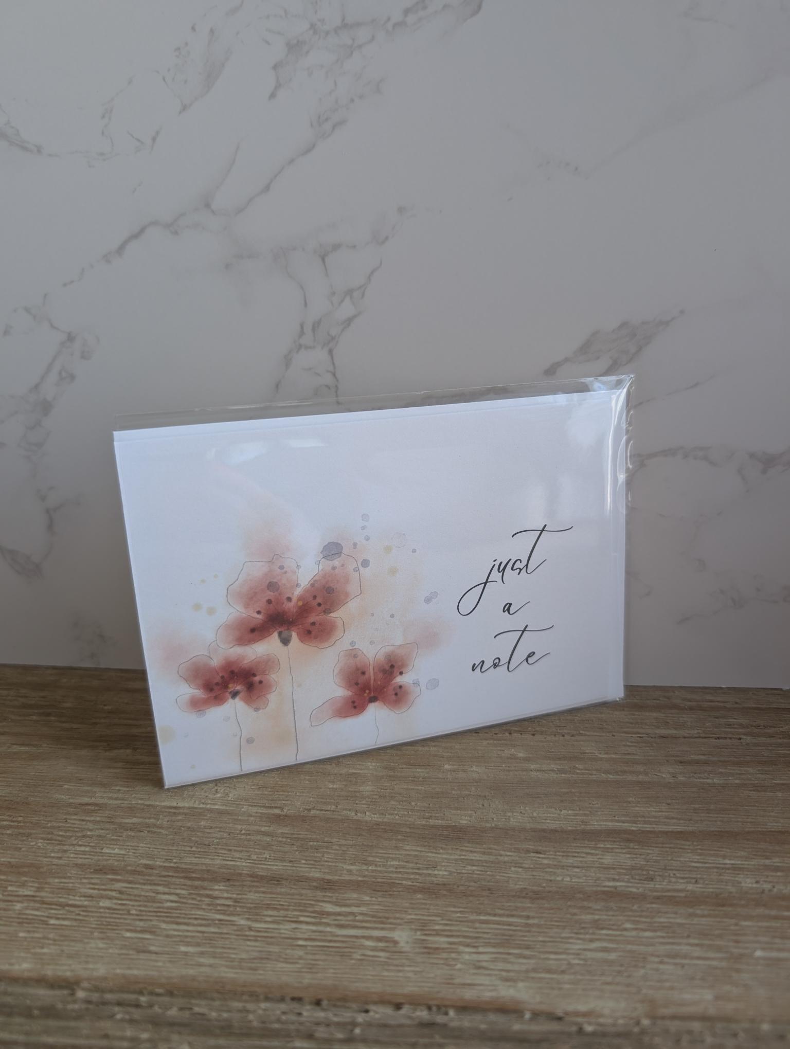 Note card with red watercolor floral design and 'just a note' text on a marble background