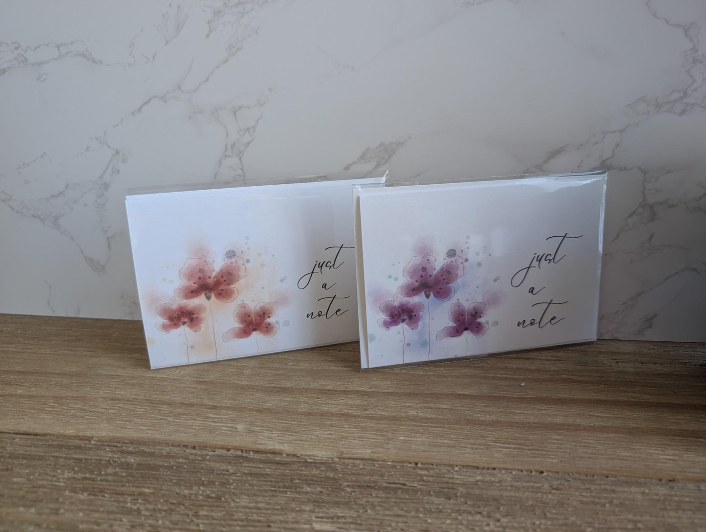 Two greeting cards with a watercolor floral designs and 'just a note' text on a marble surface.