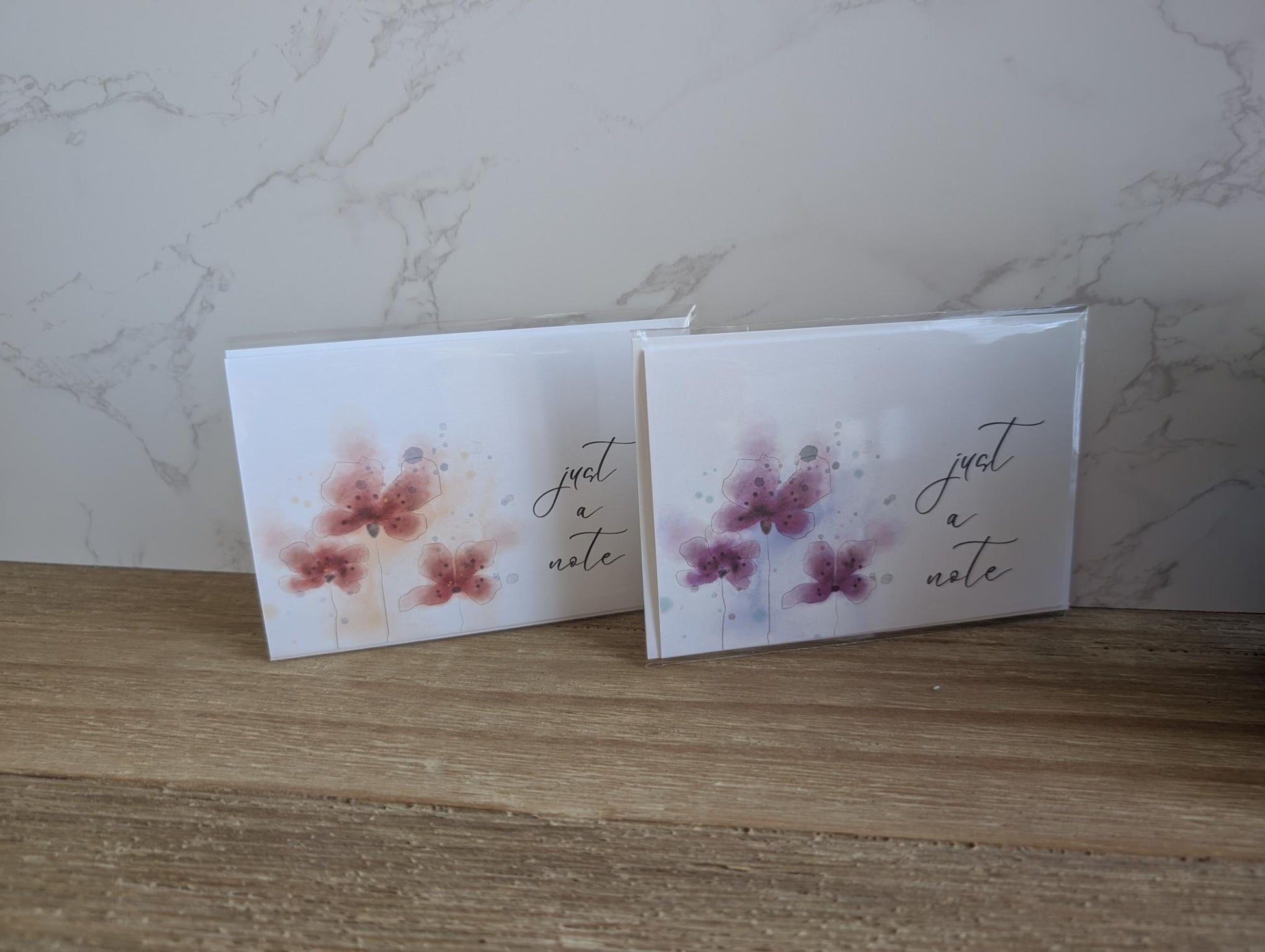 Two greeting cards with a watercolor floral designs and 'just a note' text on a marble surface.