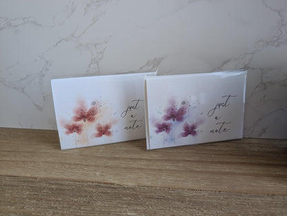 Two greeting cards with a watercolor floral designs and 'just a note' text on a marble surface.