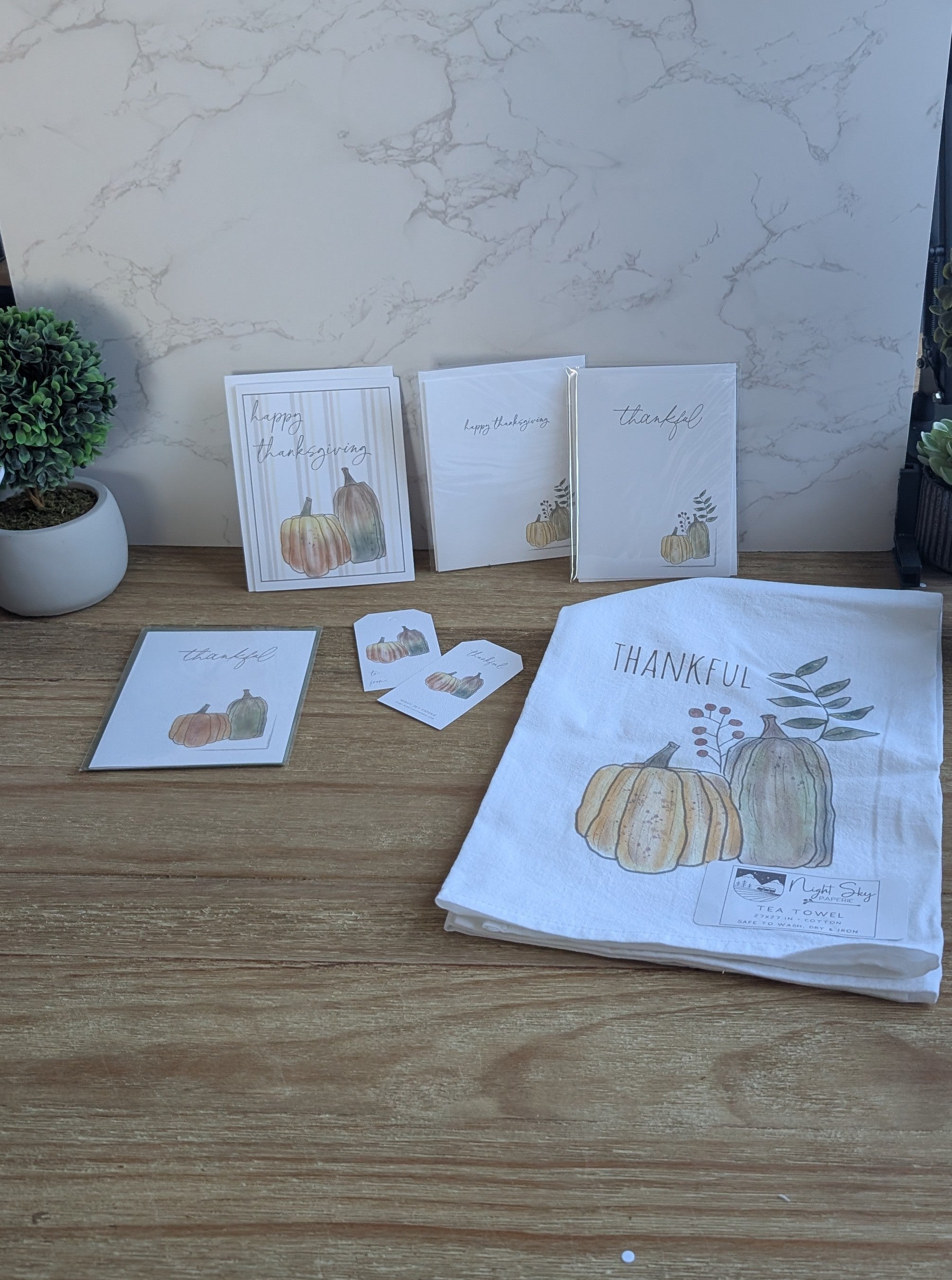 Set of greeting cards and a towel with pumpkin designs on a wooden surface.
