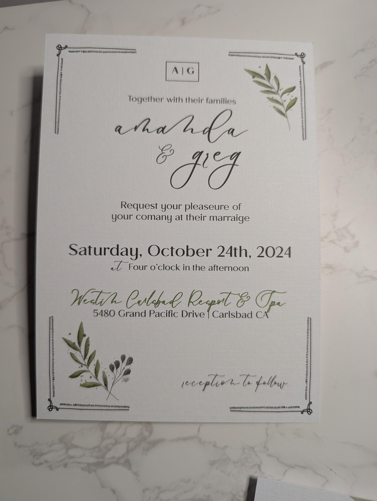 Wedding invitation card with greenery design on a marble surface