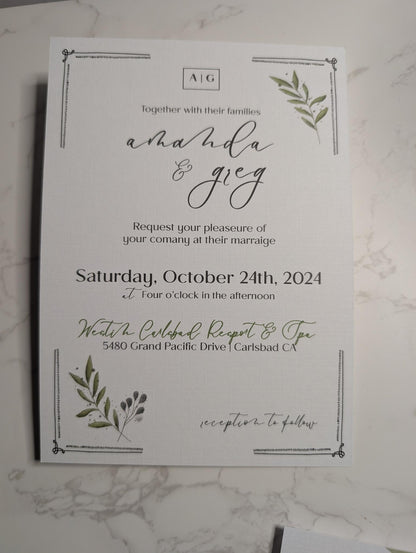 Wedding invitation card with greenery design on a marble surface