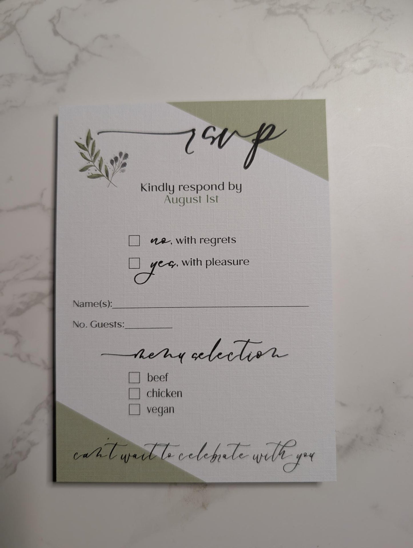 Wedding RSVP card with green accents on a marble surface