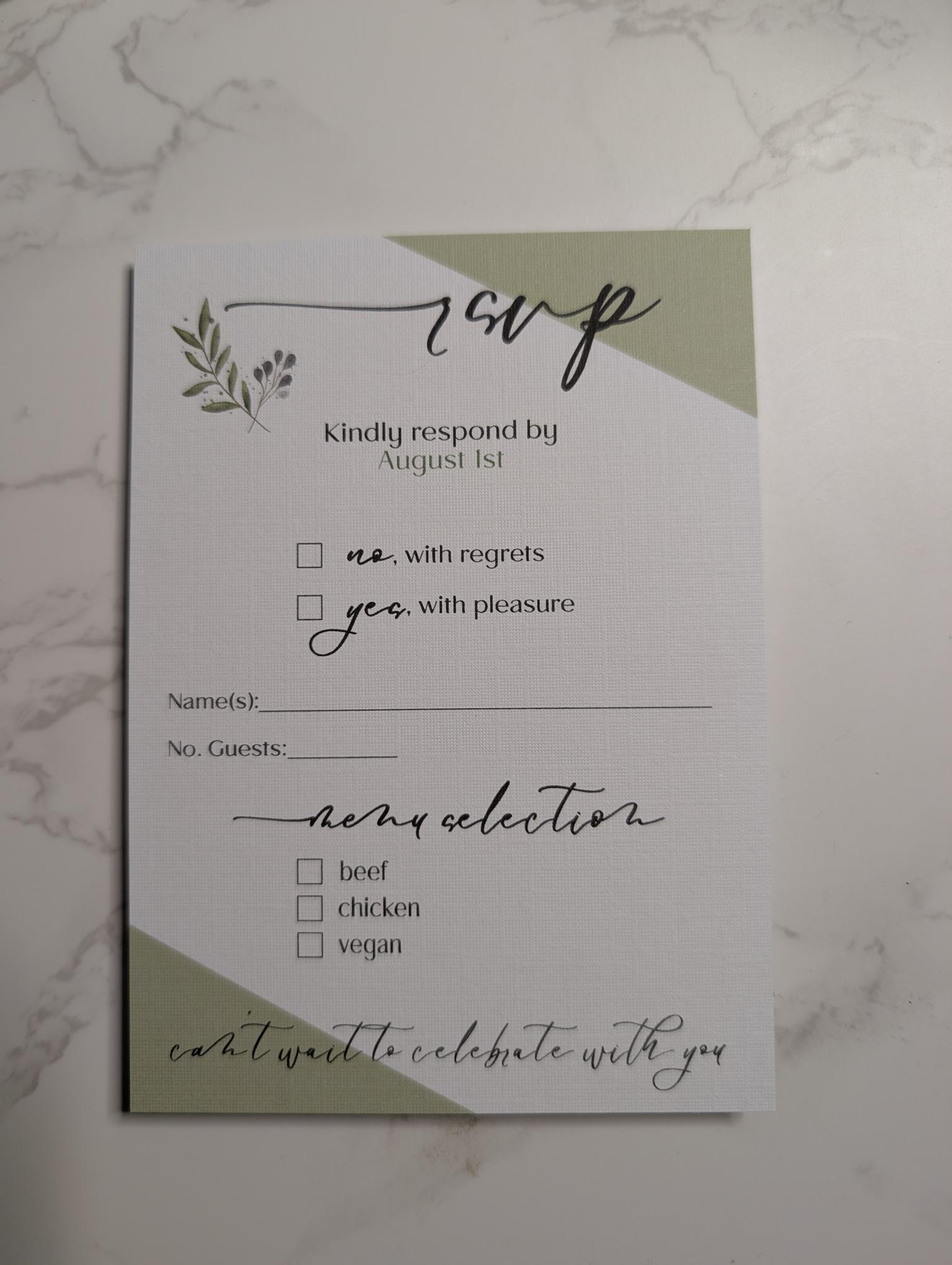 Wedding RSVP card with green accents on a marble surface