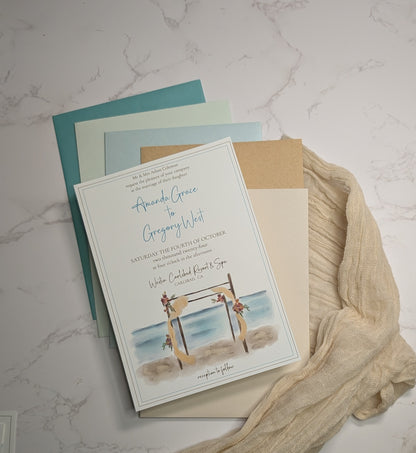 Wedding invitation card with beach scene design on a marble surface