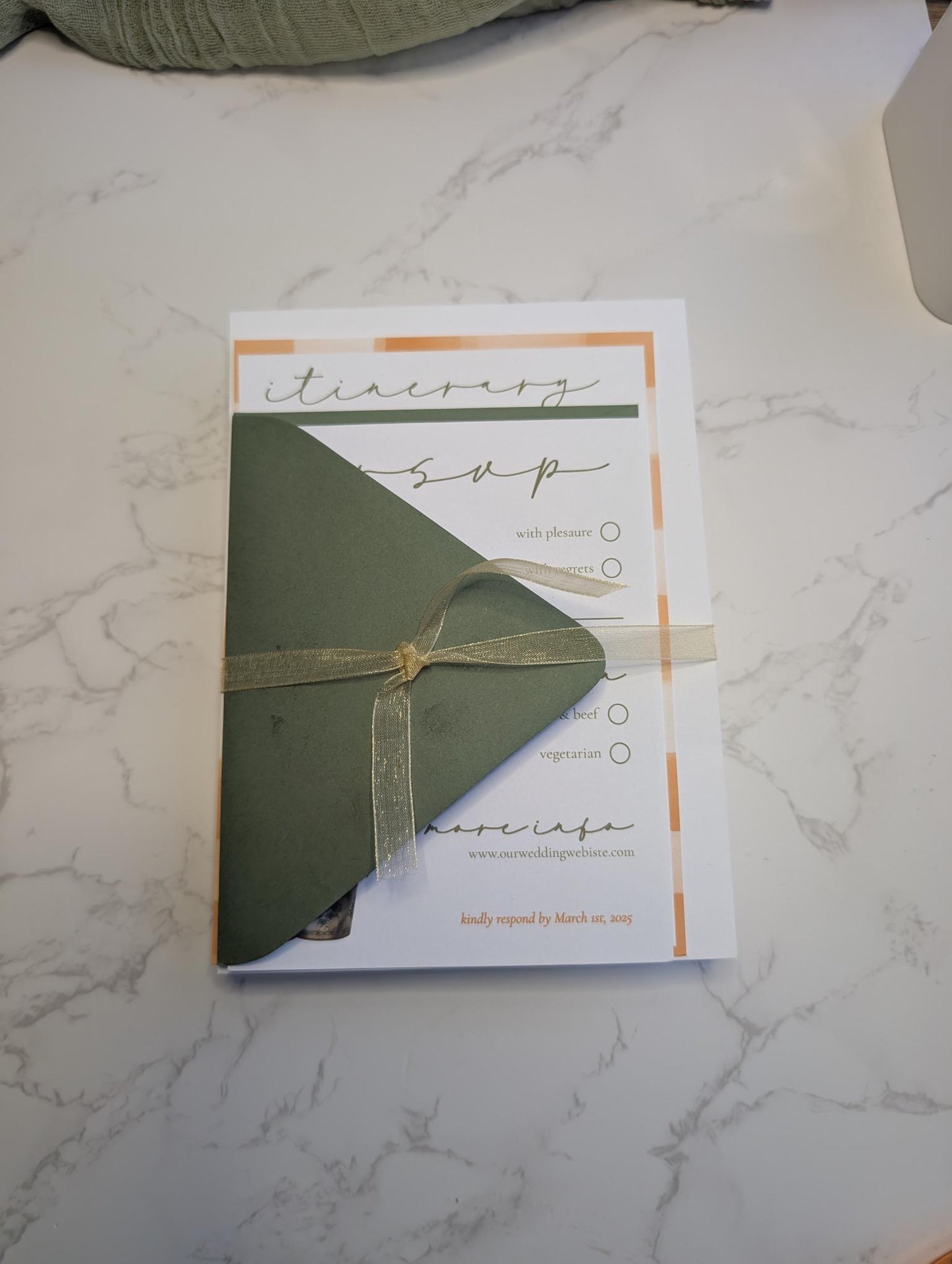 Green envelope with a gold ribbon on a white and gray marble surface