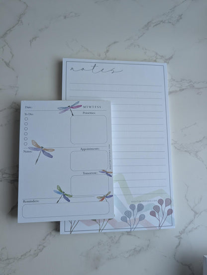Two notepads with dragonfly designs on a marble surface