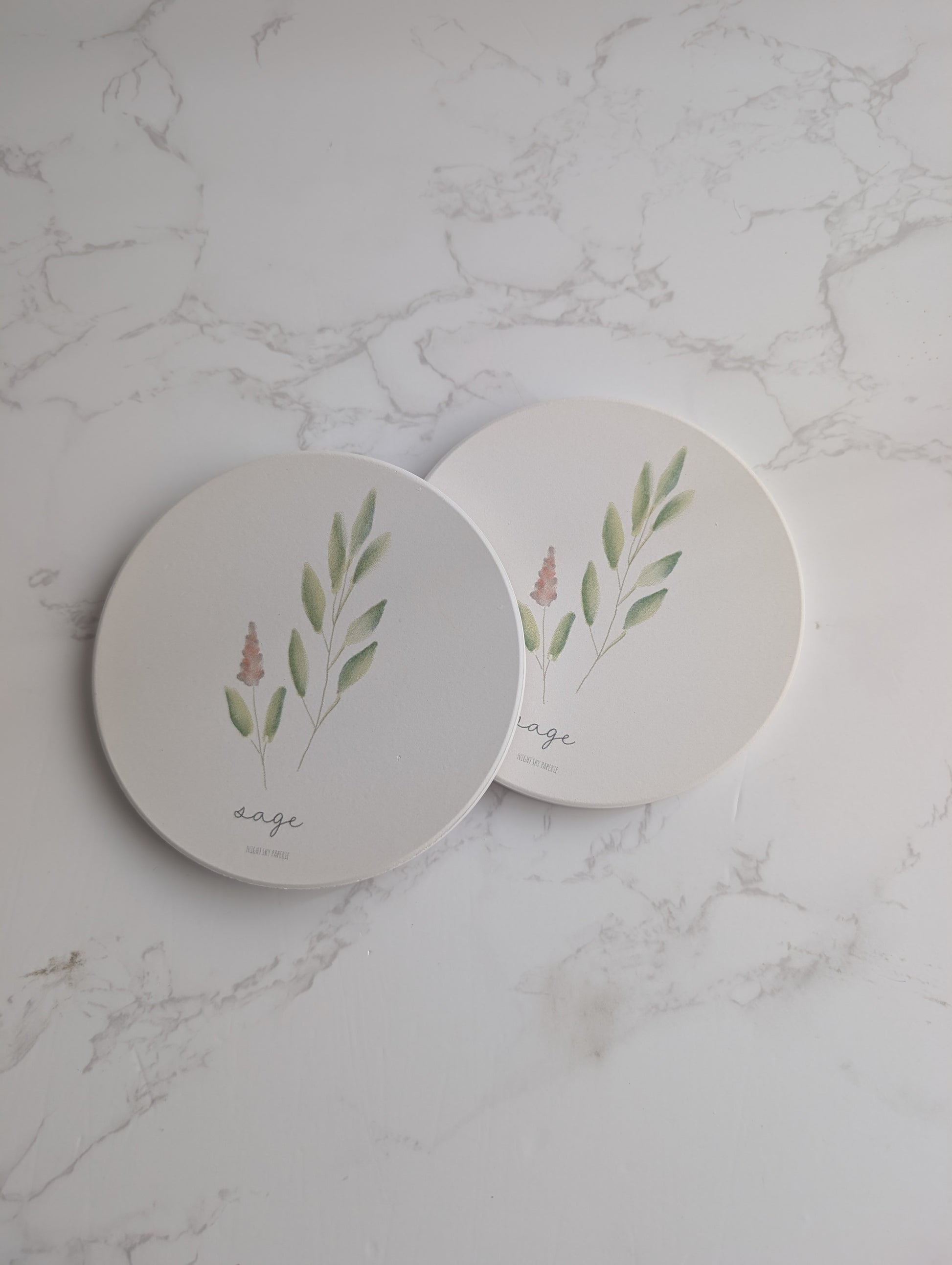 Two round ceramic coasters with plant designs on a marble surface