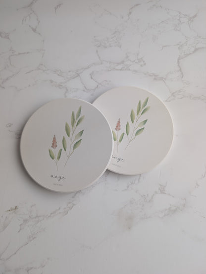 Two round ceramic coasters with plant designs on a marble surface