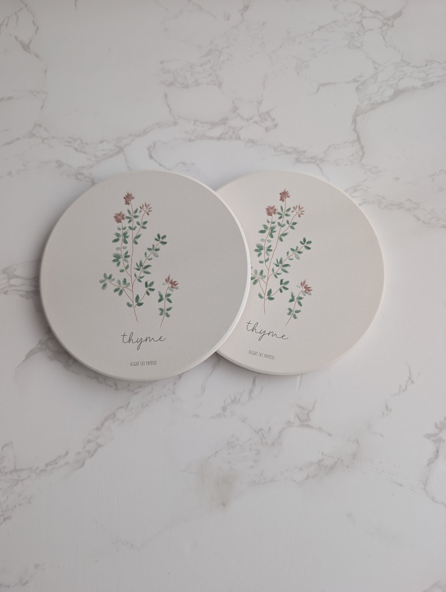 Two round ceramic plates with floral designs and the word 'thyme' on a marble surface.