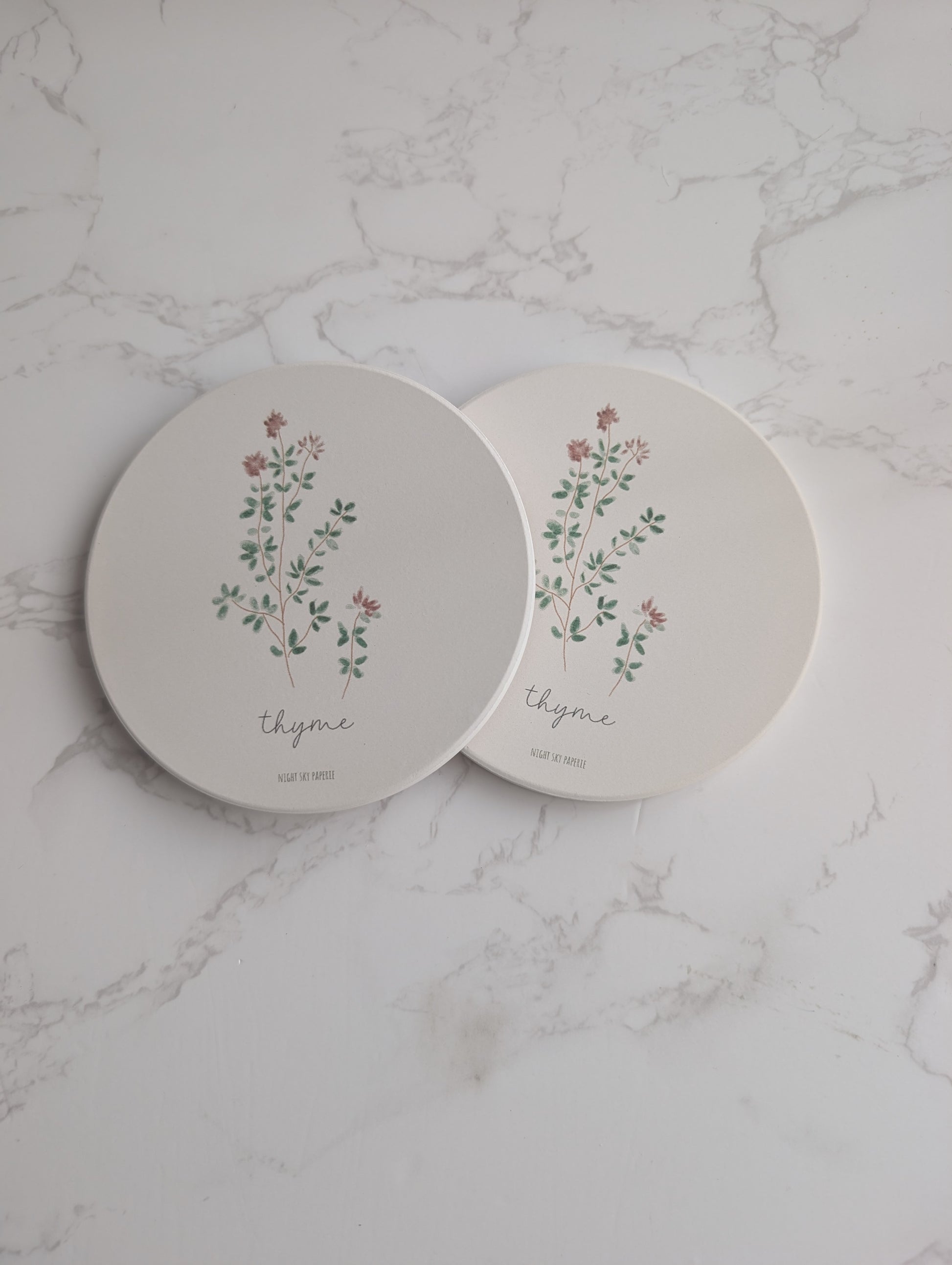 Two round ceramic plates with floral designs and the word 'thyme' on a marble surface.
