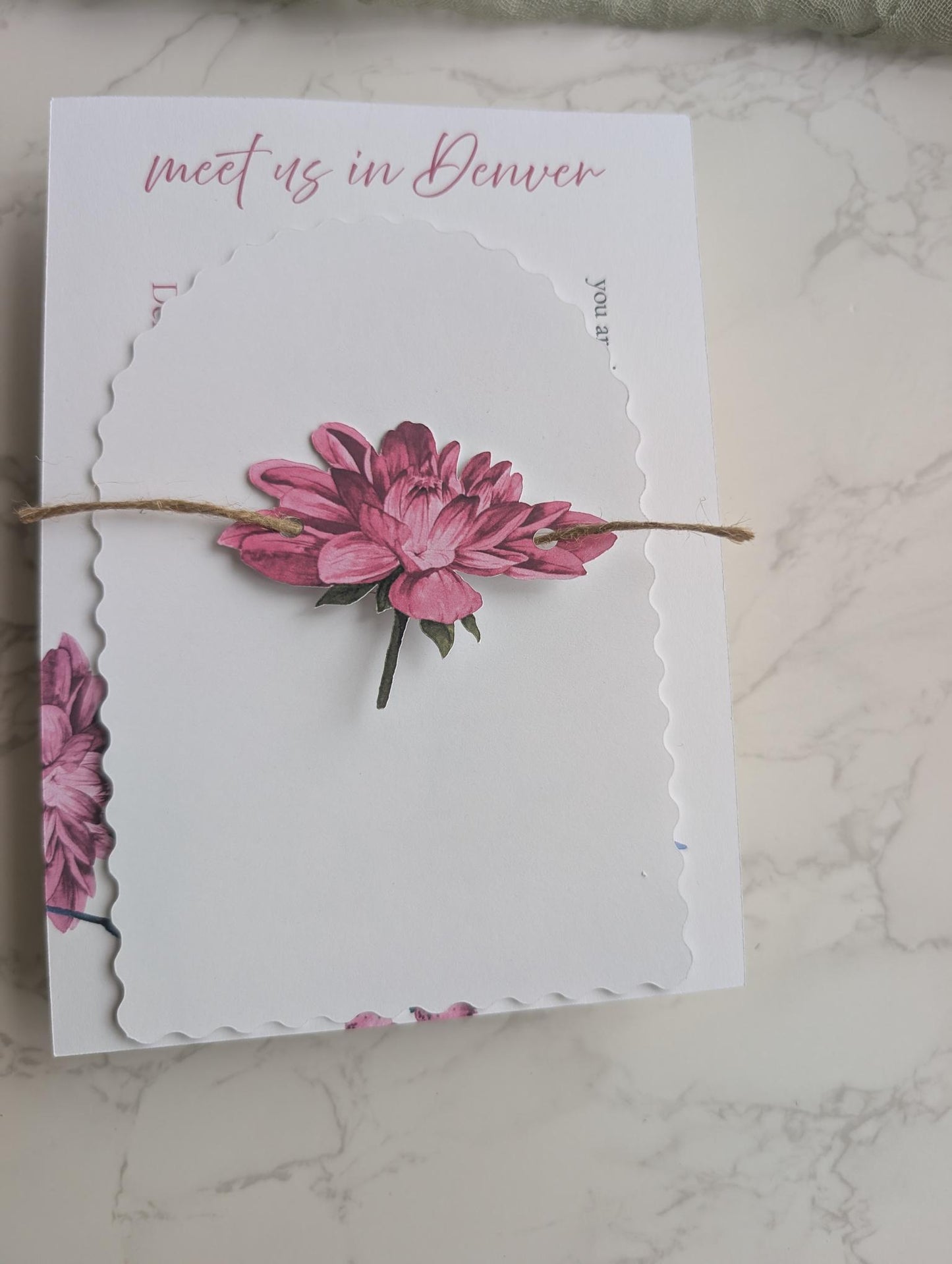 Card with pink flowers and 'meet us in Denver' text on a marble surface