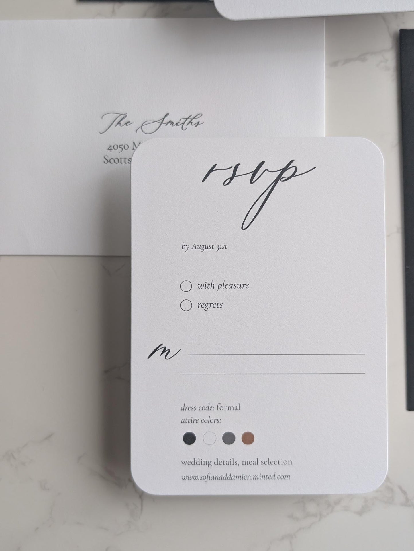 White RSVP card with black text on a marble surface