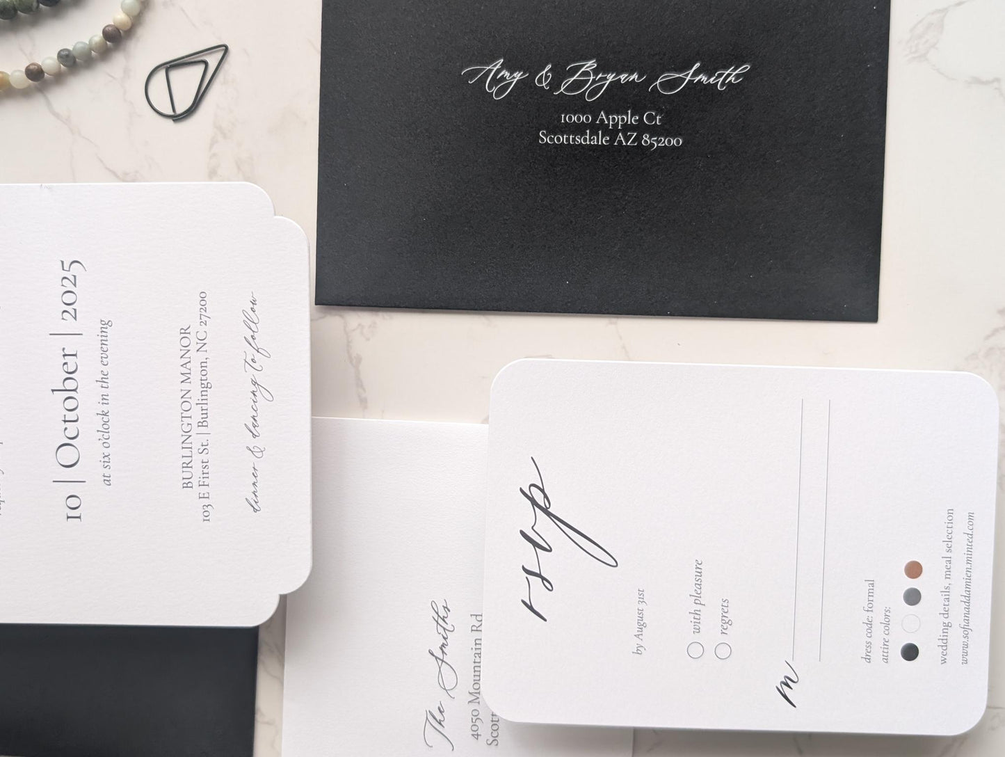 Black and white wedding invitation set on a marble surface