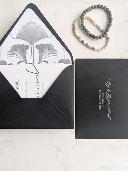 Black envelope with white interior featuring a floral design, next to a black card with white text on a light gray background.