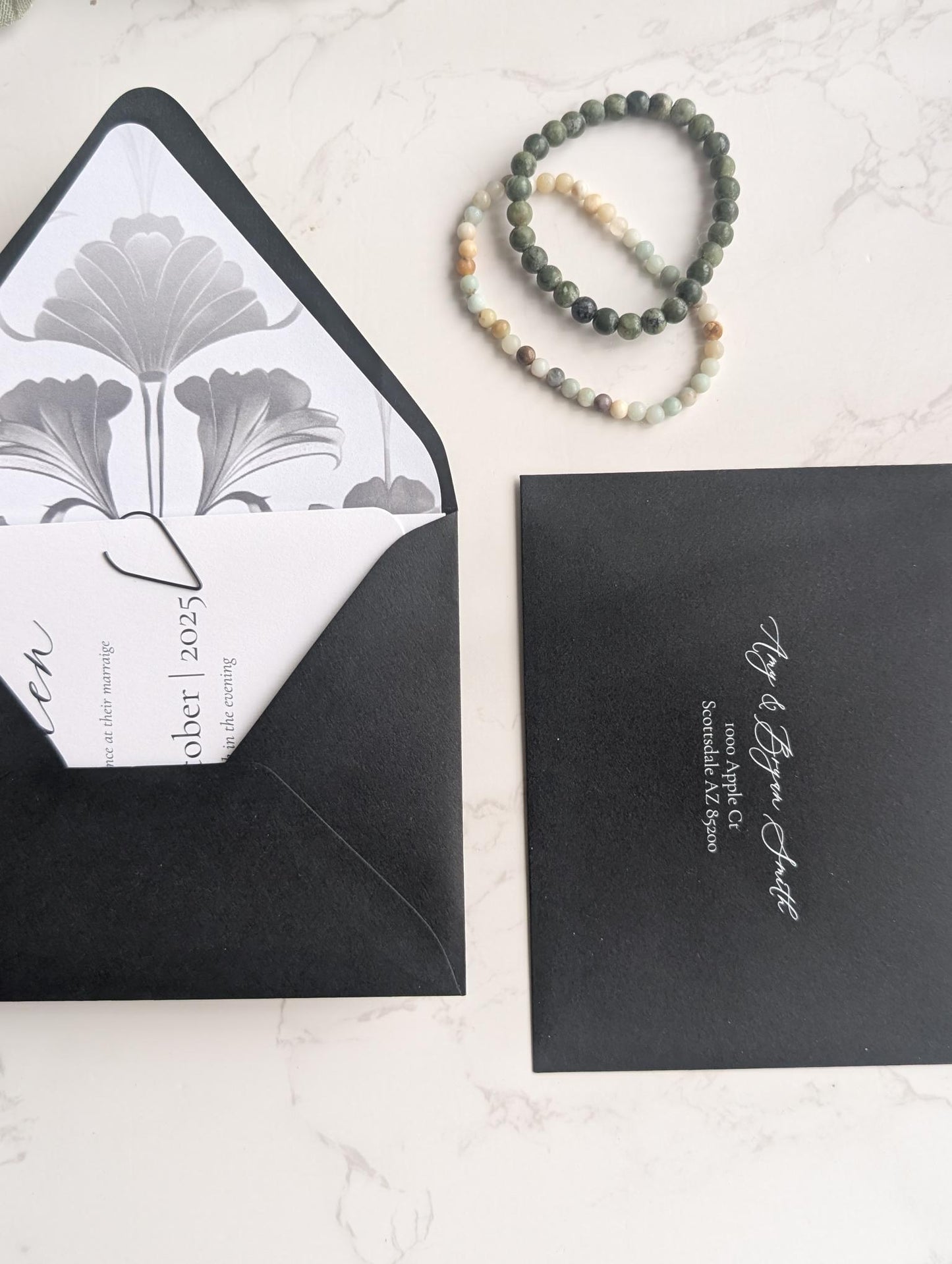 Black envelopes with white interior and floral design, accompanied by a bracelet on a light surface.