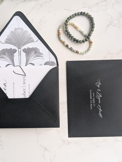 Black envelopes with white interior and floral design, accompanied by a bracelet on a light surface.