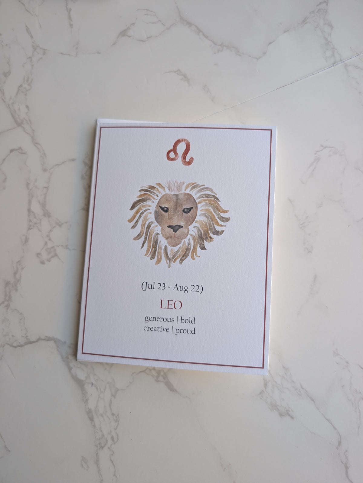 A white card featuring a watercolor lion illustration and the Leo zodiac sign, placed on a light marble surface.