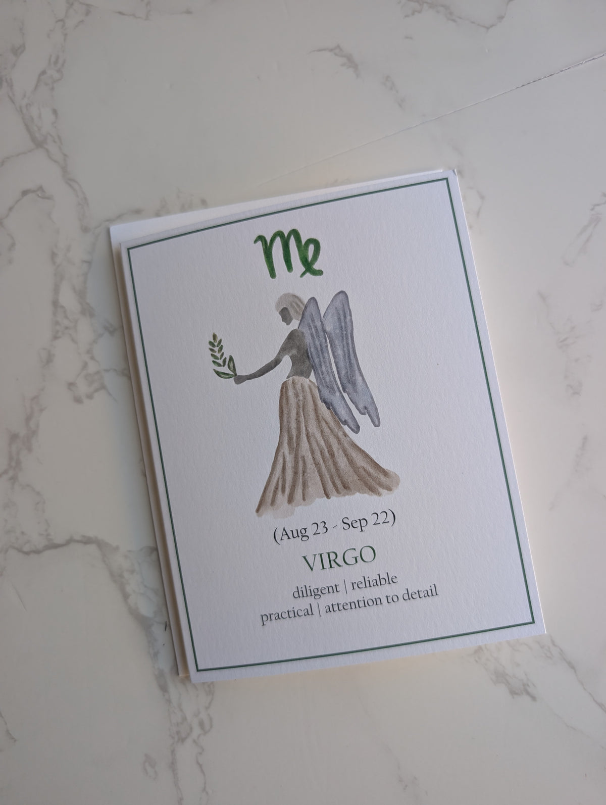 A rectangular white card featuring a watercolor-style Virgo angel illustration and the text 'Me (Aug 23 - Sep 22) VIRGO diligent | reliable | practical | attention to detail', photographed on a light marble surface.