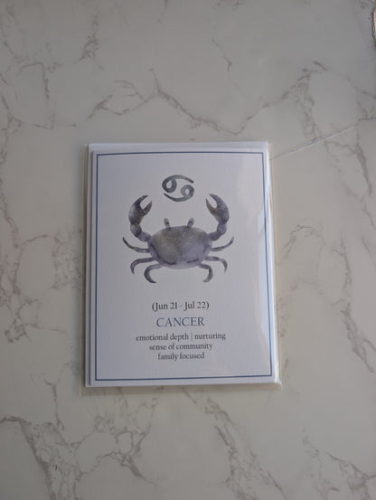 A square art print featuring a watercolor-style Cancer zodiac crab and astrological symbol, displayed on a light marble-patterned surface.