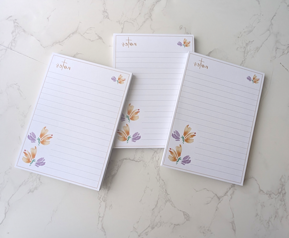 stacked loosely, three notepads with floral watercolor design, placed on a marble background