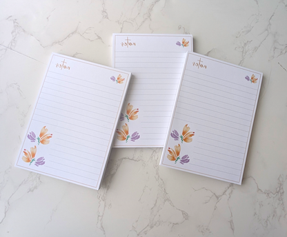 stacked loosely, three notepads with floral watercolor design, placed on a marble background