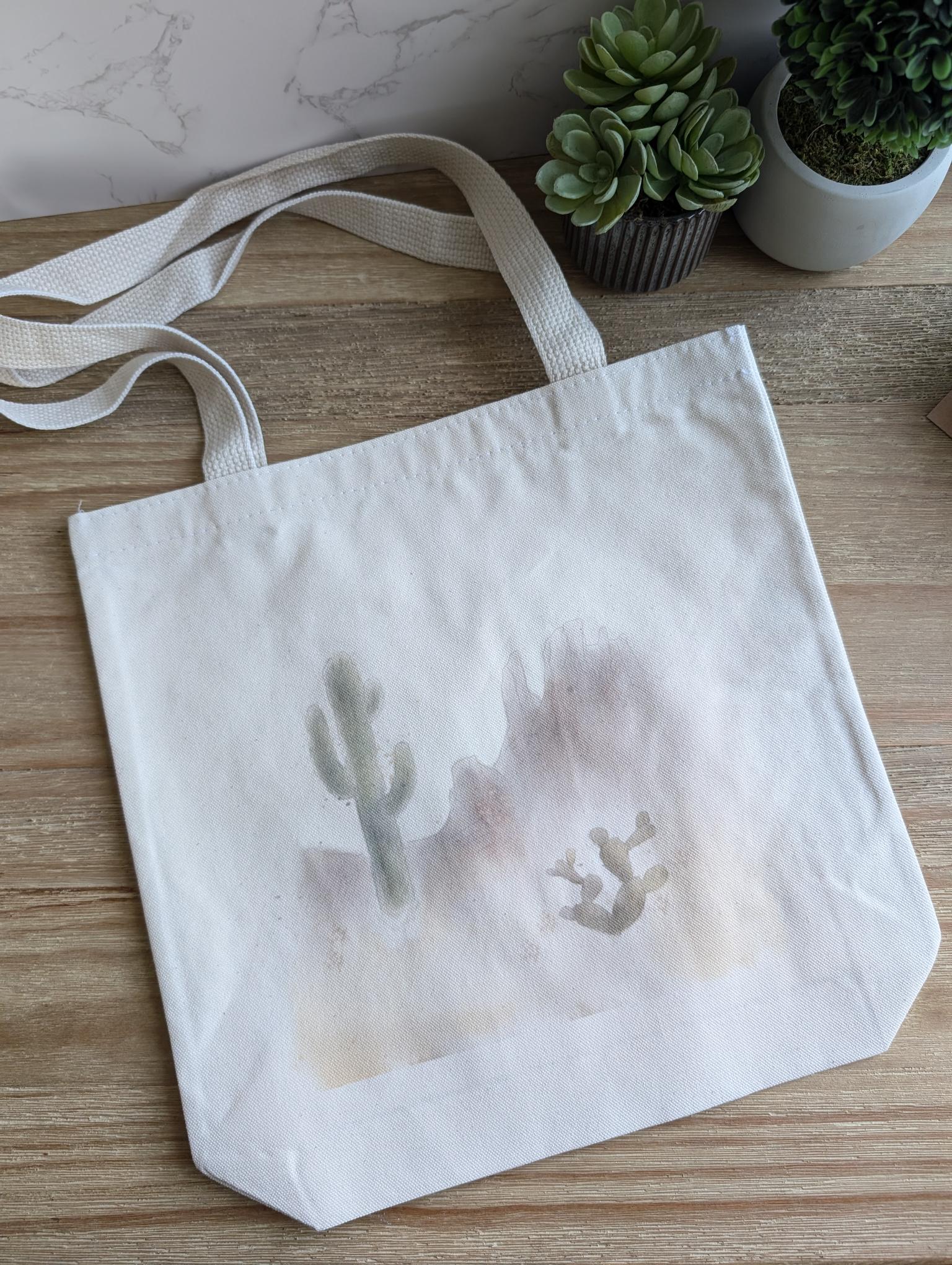 A  cotton canvas tote bag with custom watercolor desert landscape design.