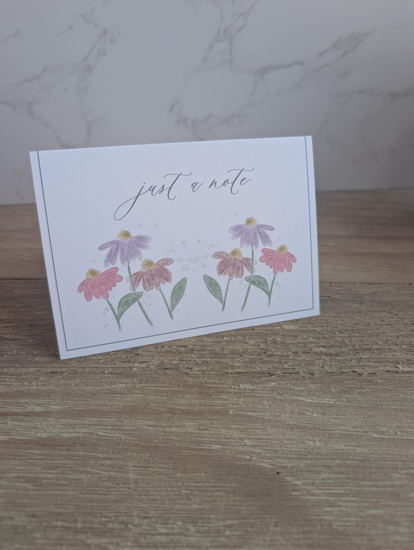 Note card with floral design and 'just a note' text on a wooden surface.