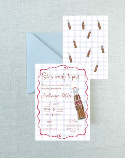 A baby shower invitation card with a retro Coca-Cola bottle illustration and pink script text, shown with a light blue envelope on a textured light gray background. A second copy of the invitation is visible behind it.