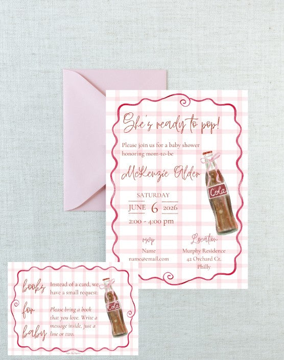 A baby shower invitation card with a pink gingham border and a retro cola bottle illustration, shown with a matching pink envelope on a light textured fabric background. A smaller matching card is placed in the lower left corner.