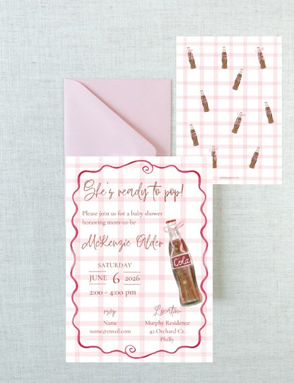 A baby shower invitation card with a pink gingham background, pink script text, a pink border, and a vintage Coca-Cola bottle illustration, shown with a matching pale pink envelope on a light gray textured background. A second view of the invitation pattern appears in the upper right.