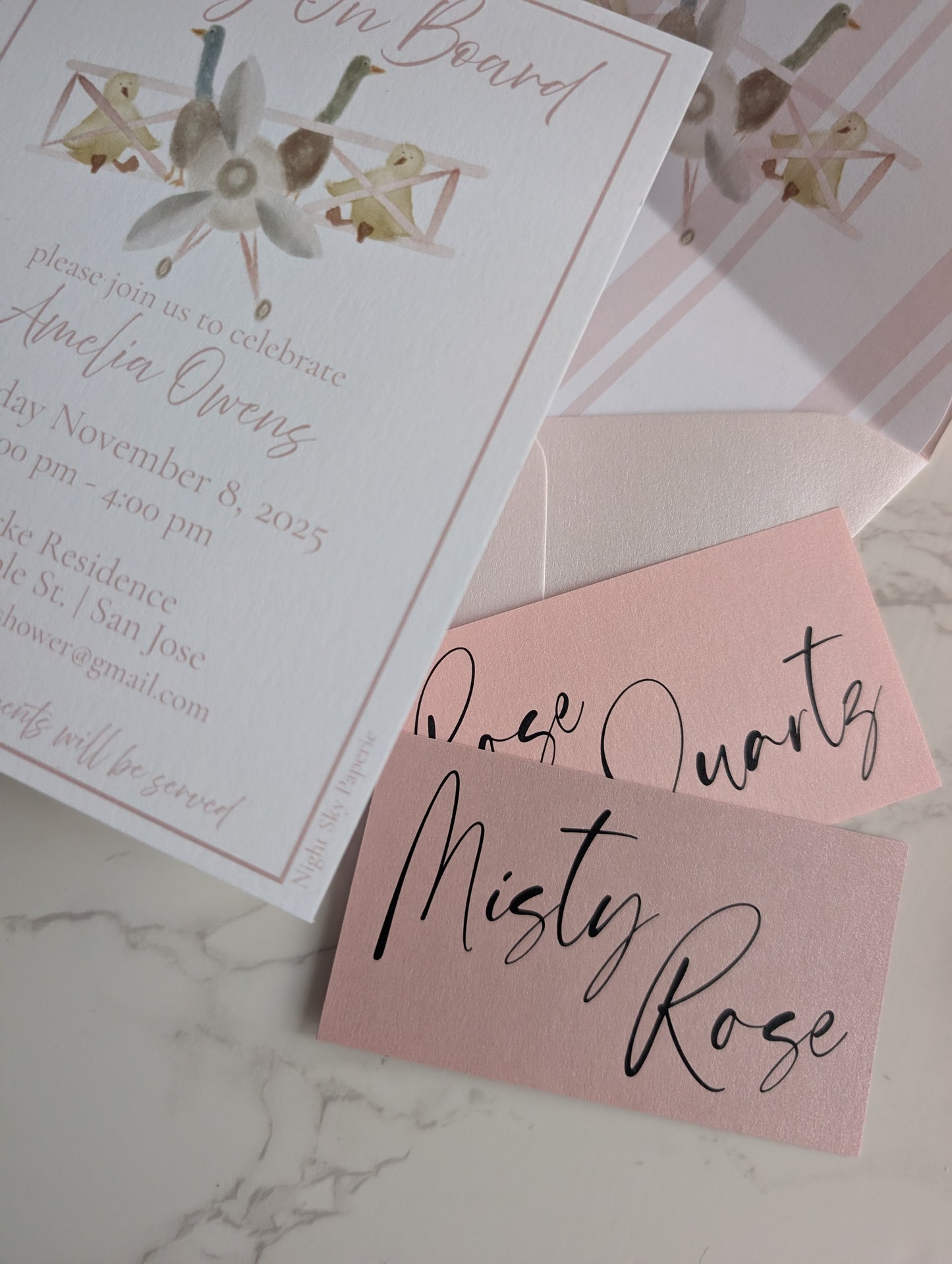 Baby shower invitation with pink envelope and 'Misty Rose' text on marble surface