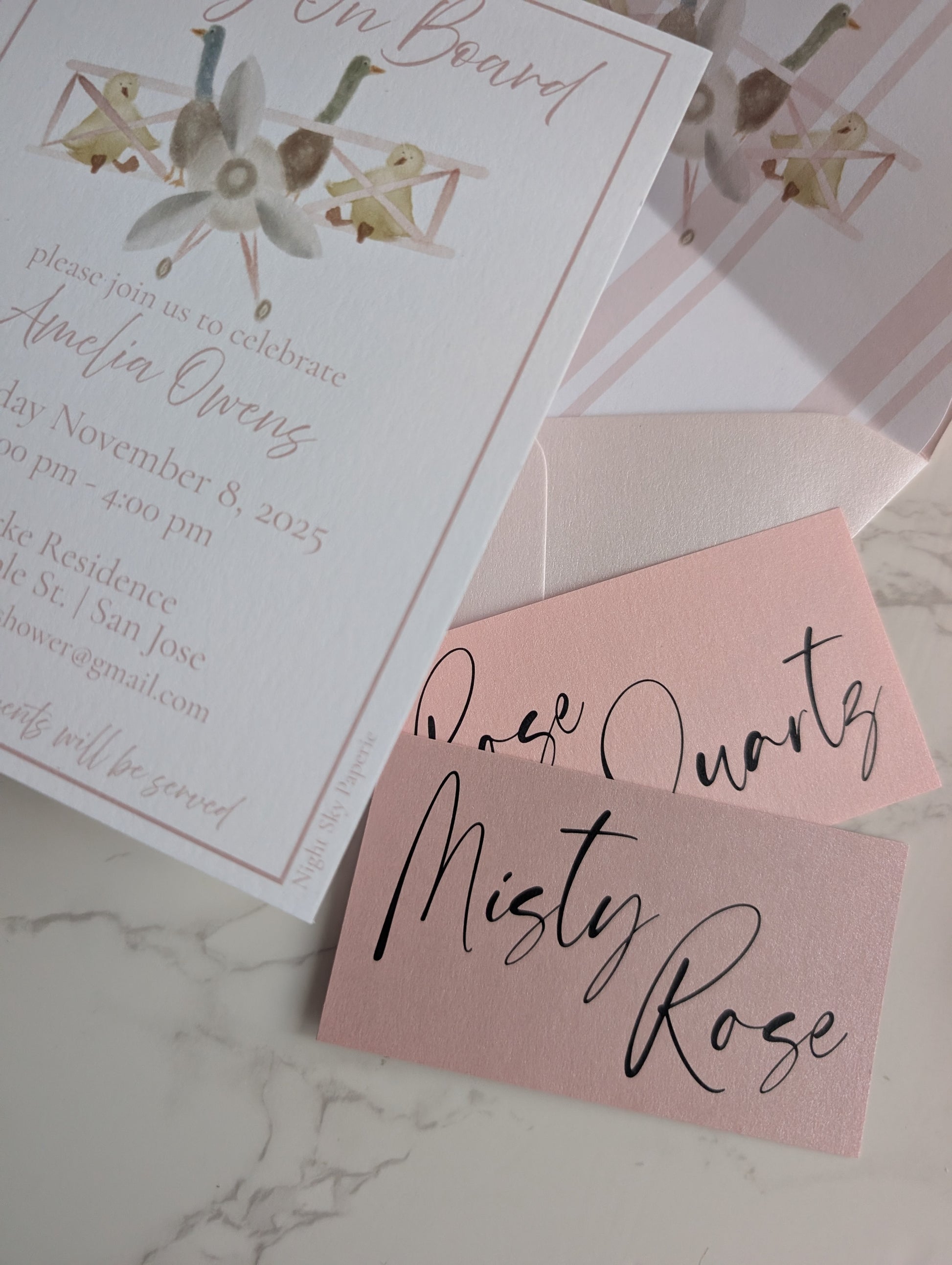 Baby shower invitation with pink envelope and 'Misty Rose' text on marble surface
