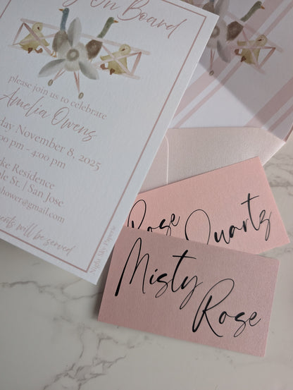 Baby shower invitation with pink envelope and 'Misty Rose' text on marble surface
