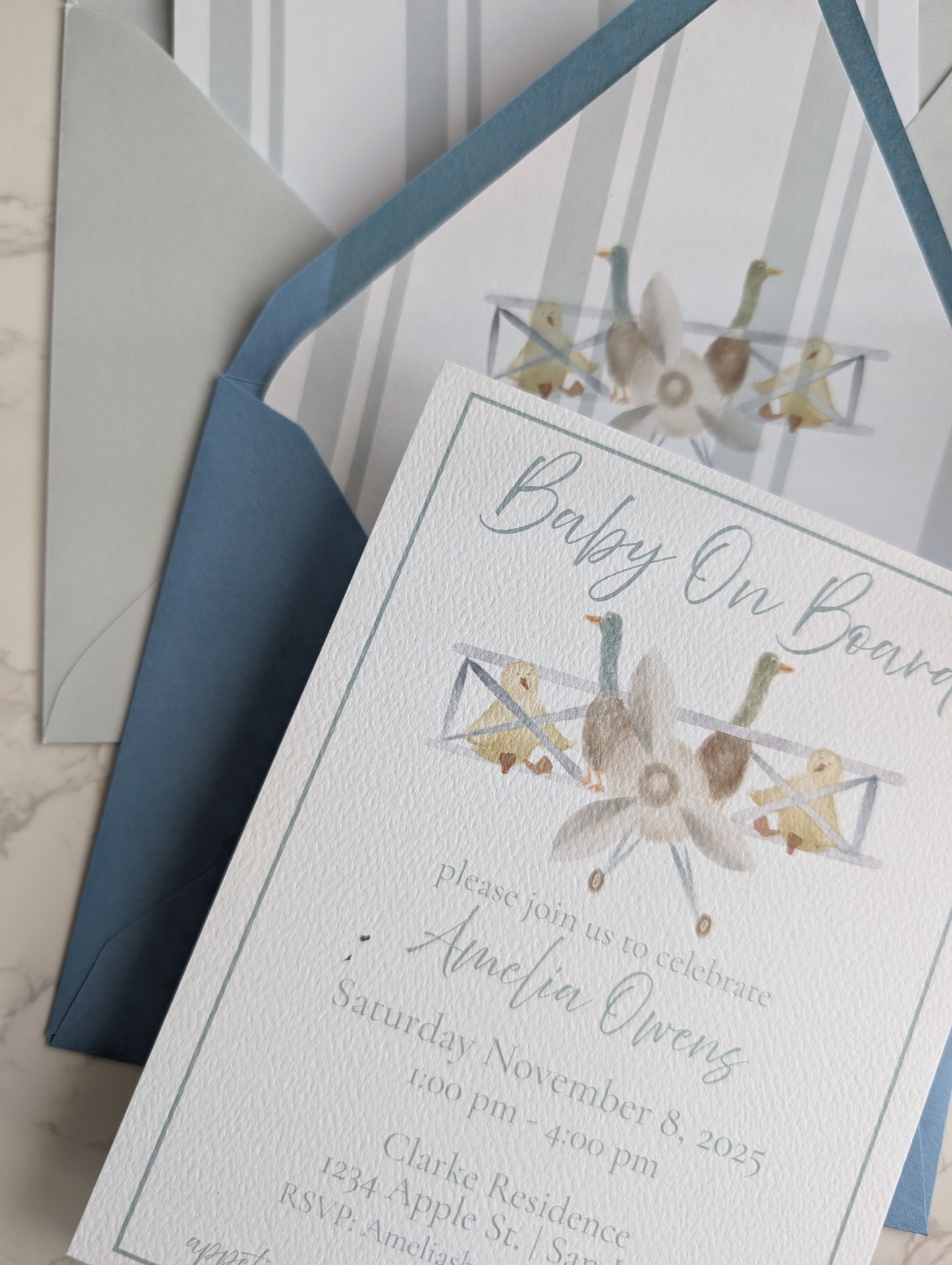 Baby shower invitation with geometric design and blue envelope on marble surface