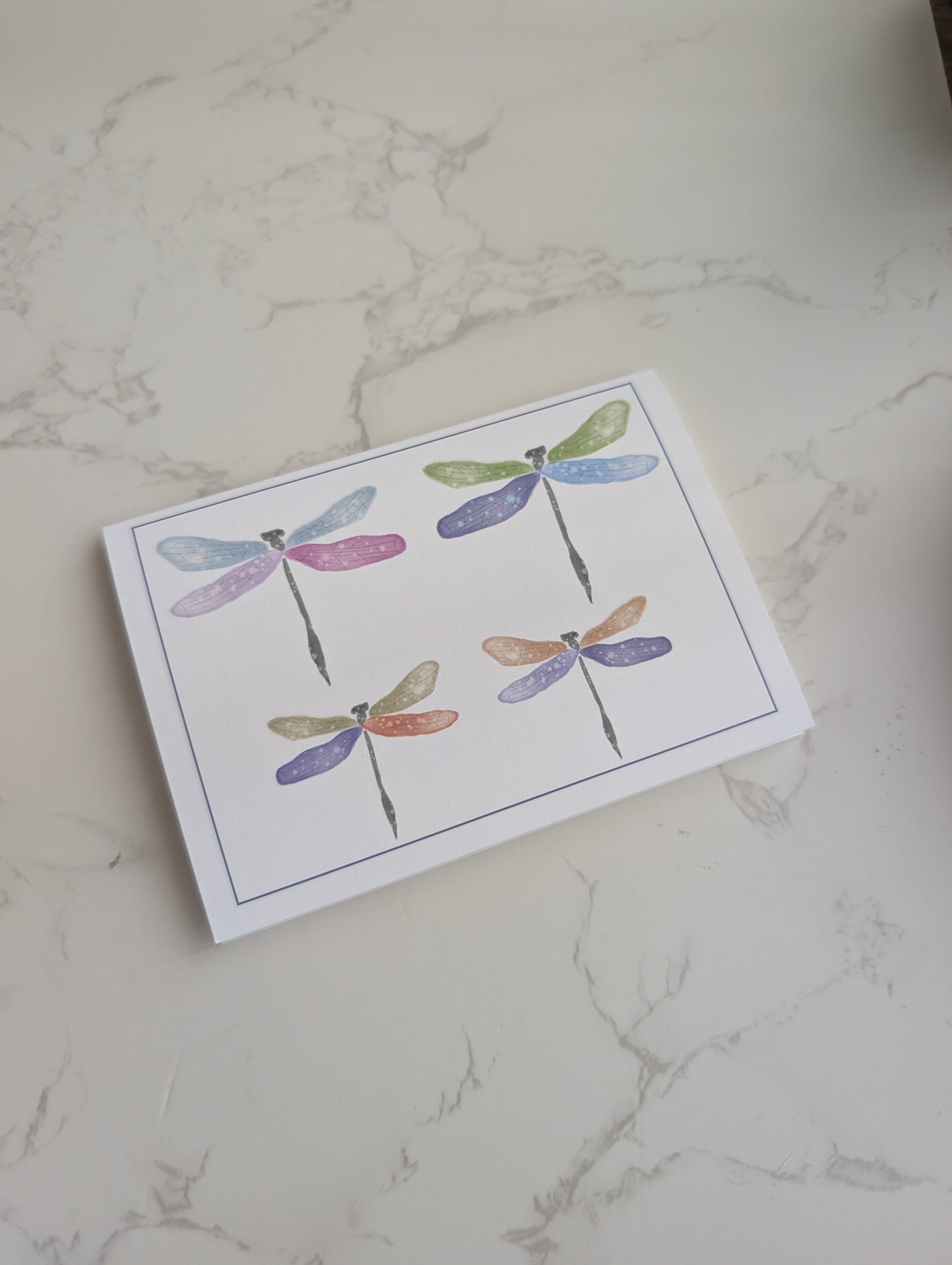 Note card with colorful dragonfly illustrations on a marble surface