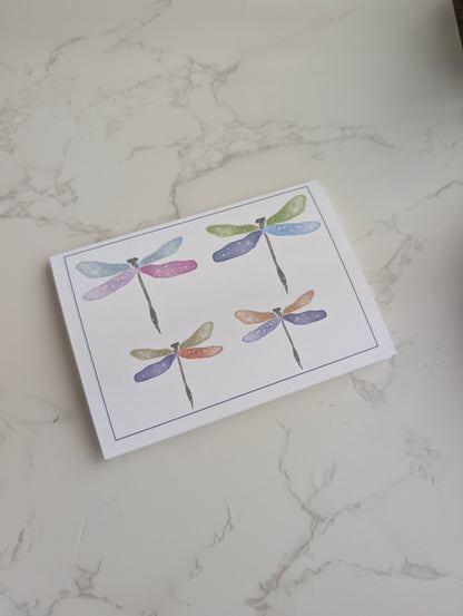 Note card with colorful dragonfly illustrations on a marble surface