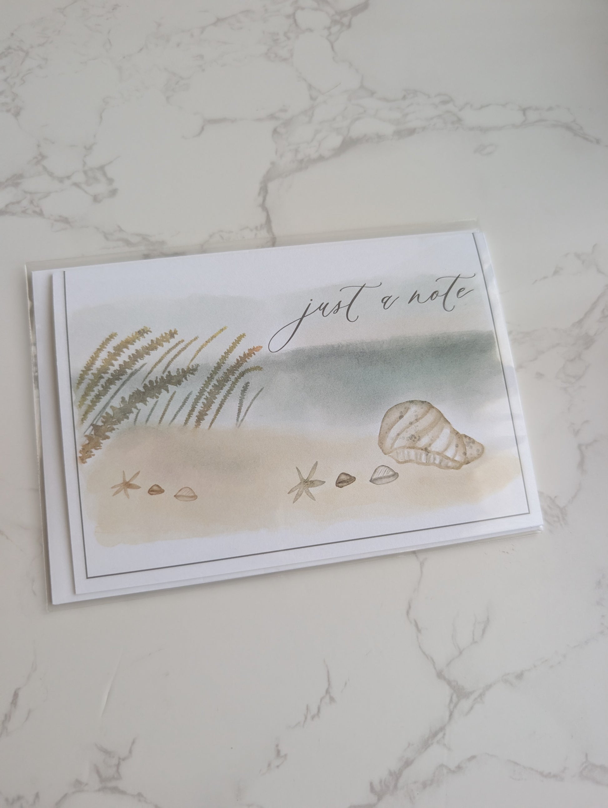 Note card with beach scene illustration and 'just a note' text on marble surface