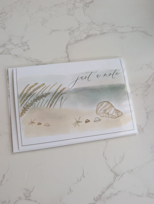 Note card with beach scene illustration and 'just a note' text on marble surface
