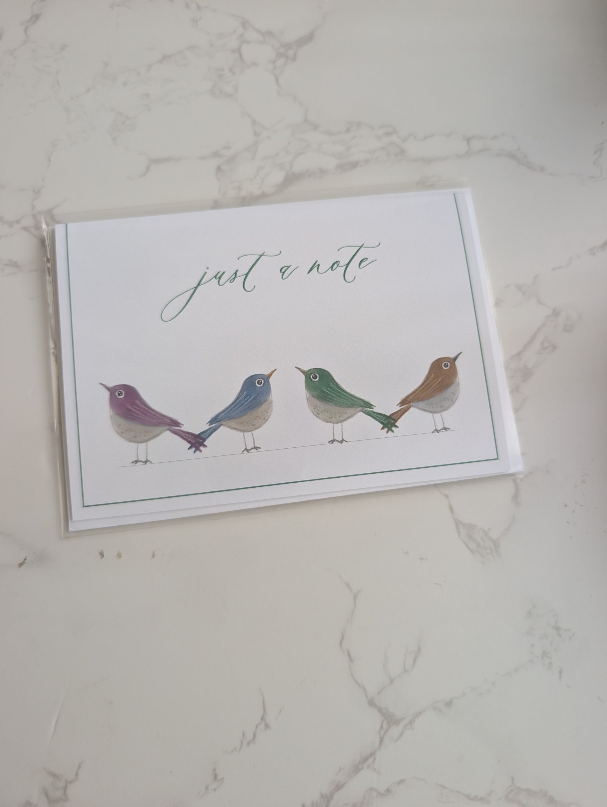 Note card with birds illustration and 'just a note' text on a marble surface