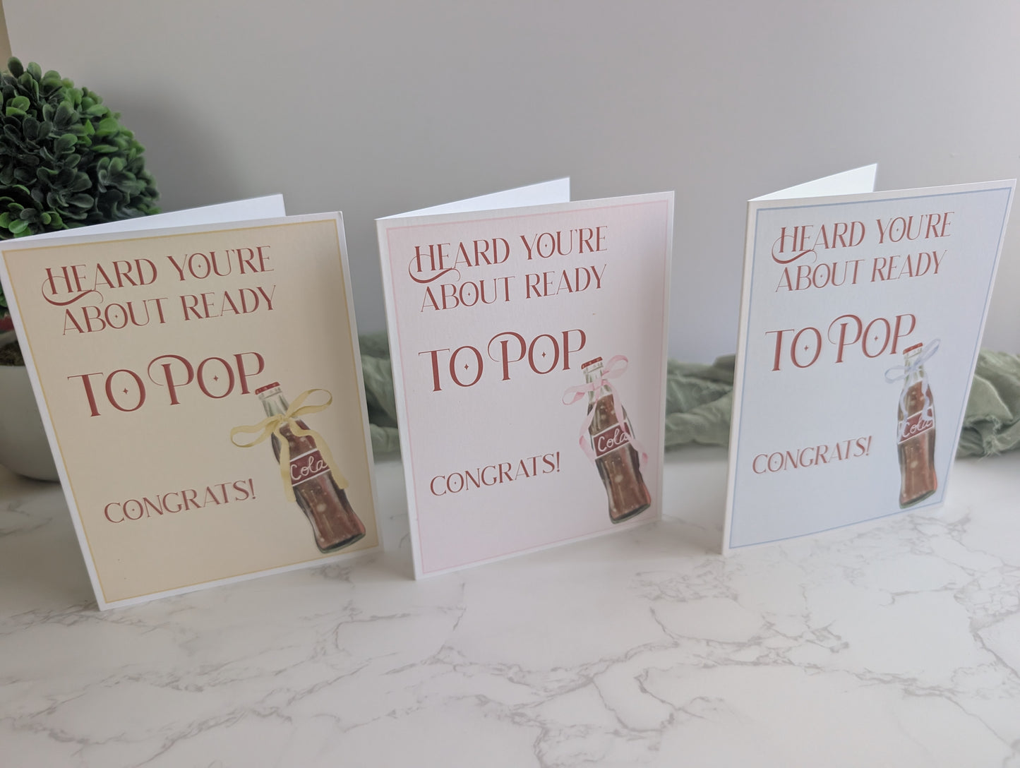 Three baby shower cards with a bottle design on a marble surface.