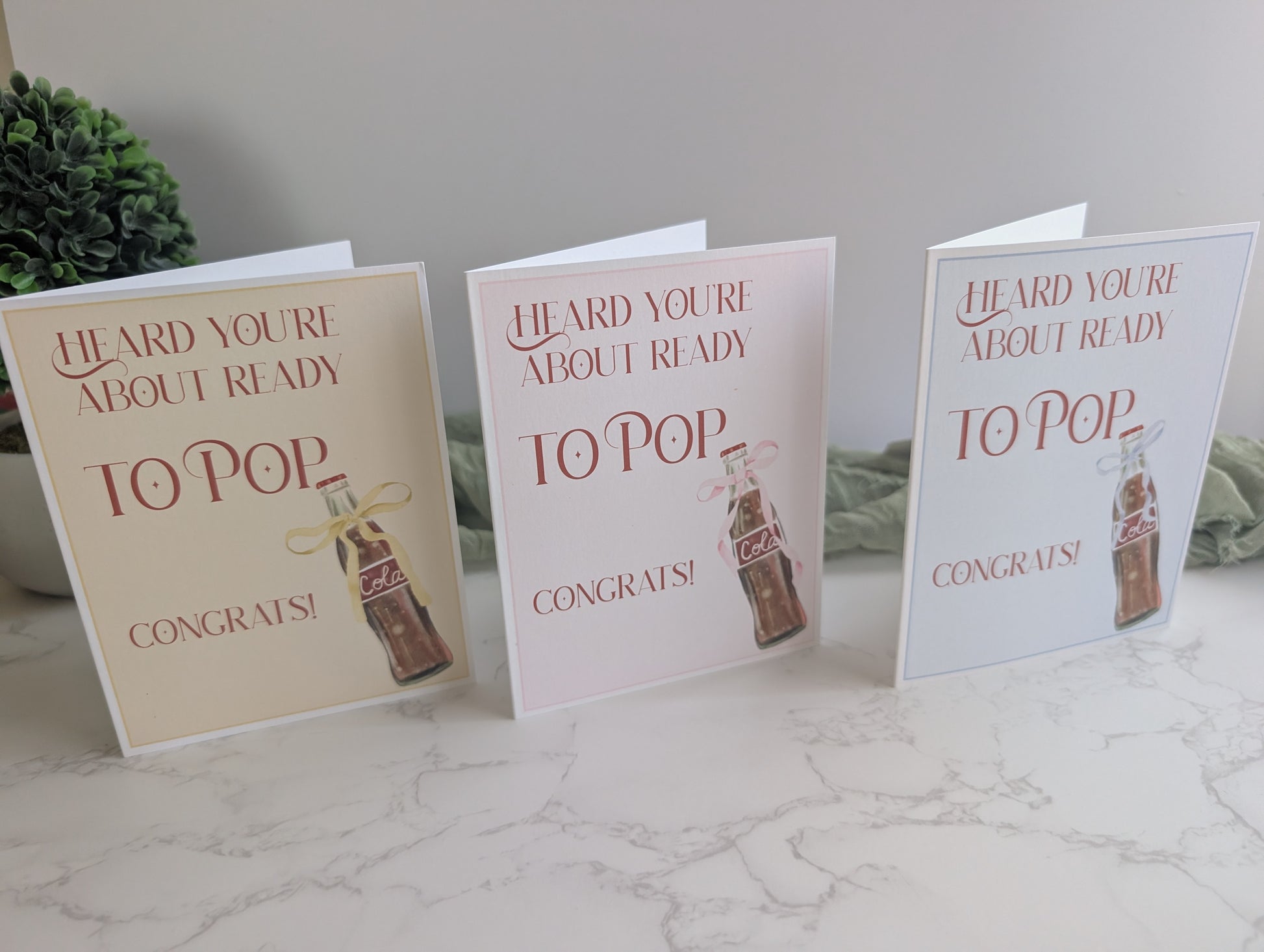 Three baby shower cards with a bottle design on a marble surface.