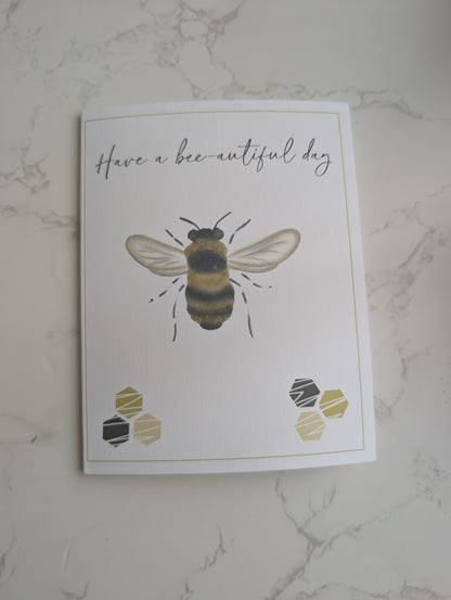 Greeting card with a bee illustration and 'Have a bee-autiful day' text on a marble surface.