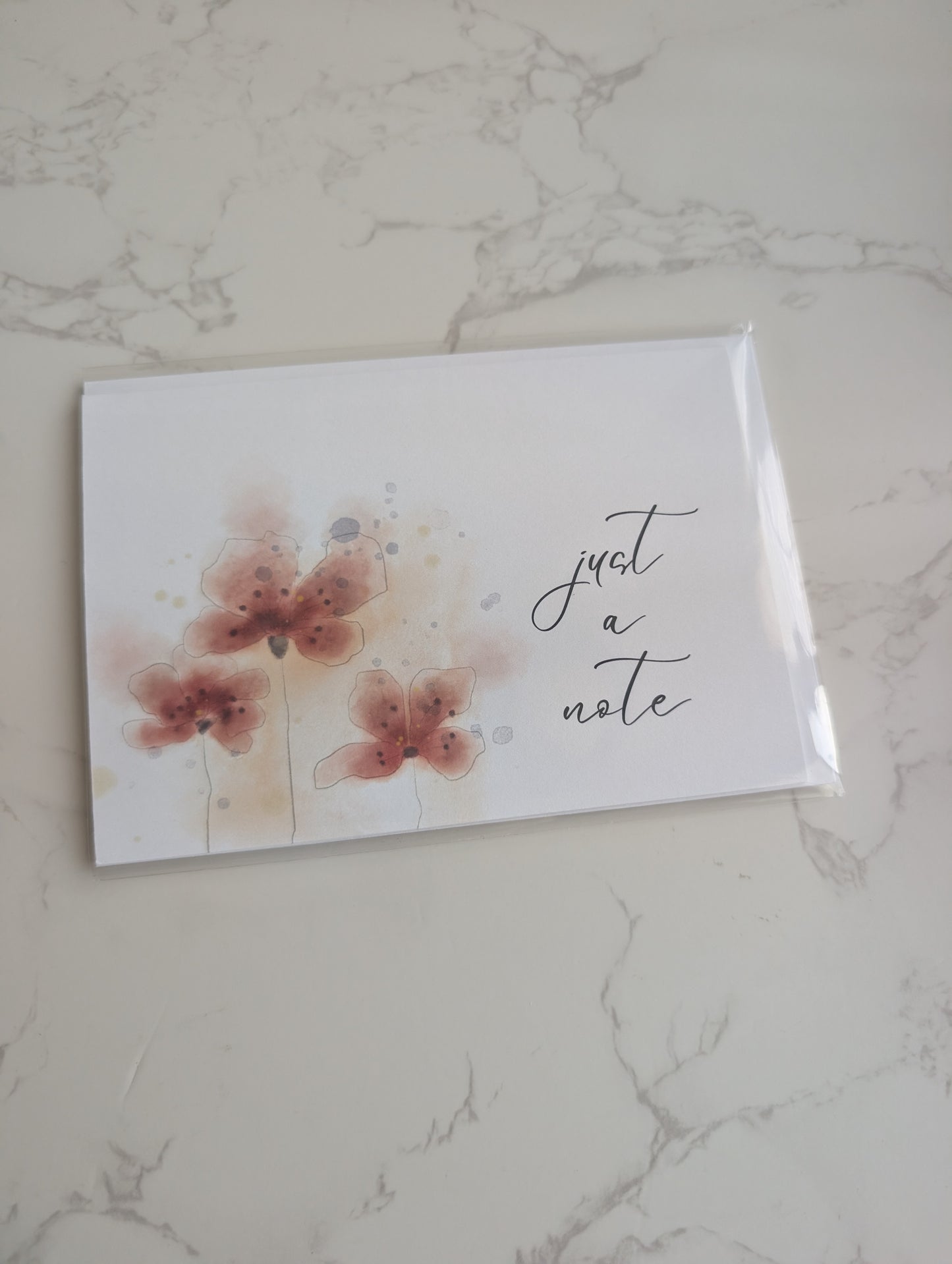 Note card with floral design and 'just a note' text on a marble surface
